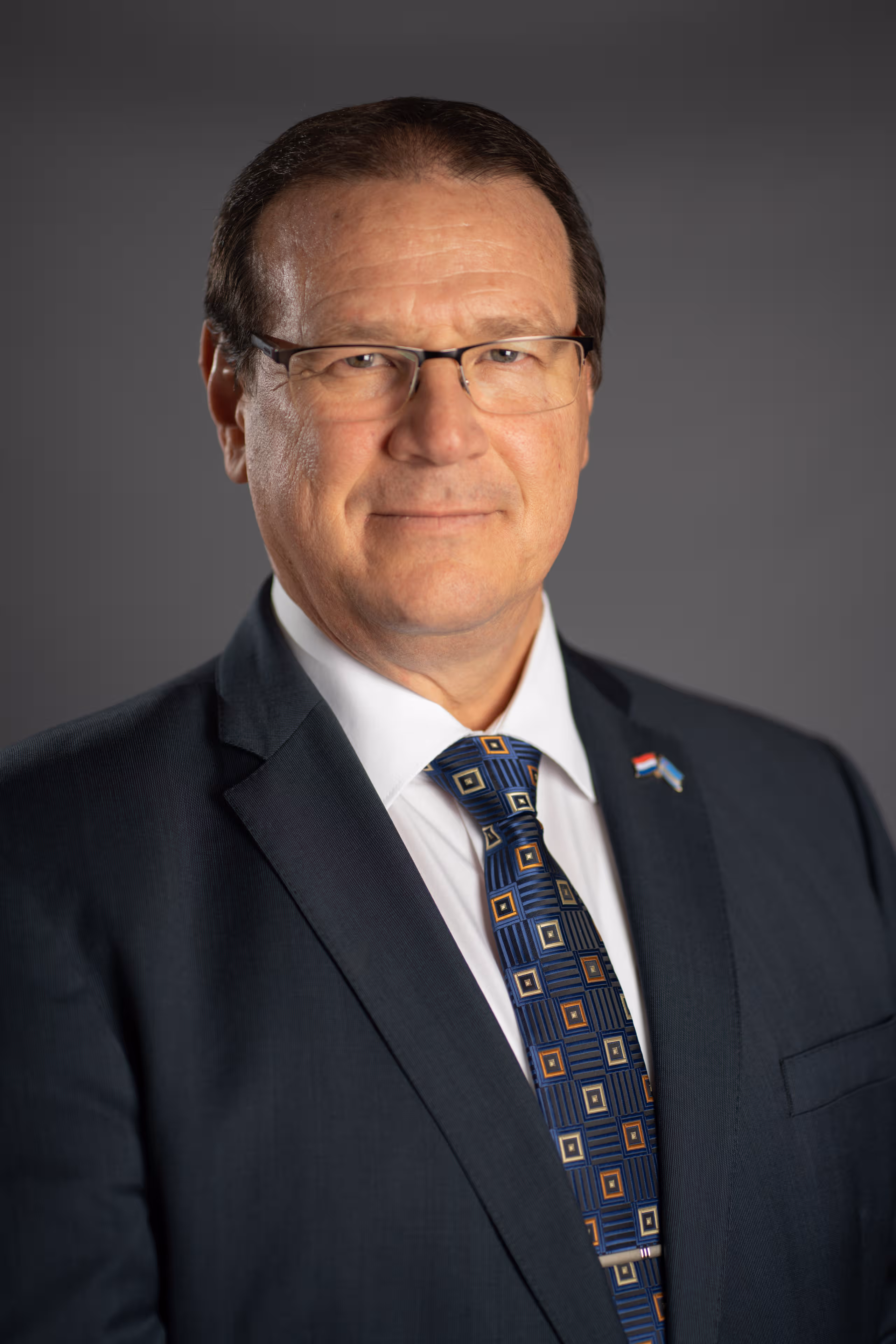 Een portretfoto van de Gouverneur van Aruba, Zijne Excellentie Alfonso Boekhoudt, voor een donkergrijze achtergrond.